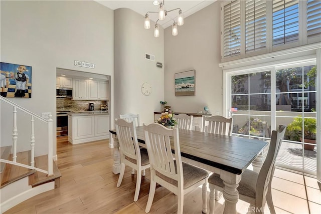 dining area with visible vents, light wood-style flooring, and a towering ceiling