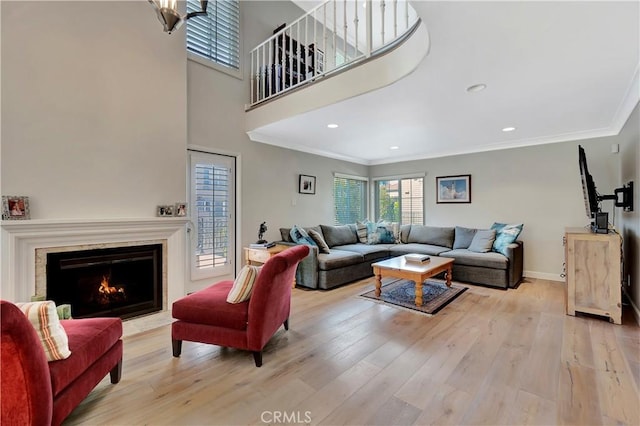 living area featuring a high end fireplace, ornamental molding, and light wood-style flooring