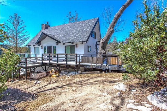 back of property with a chimney, a wooden deck, a shingled roof, and stucco siding
