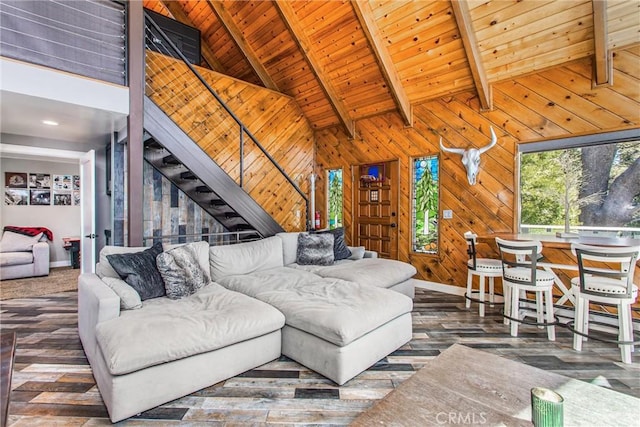 living room featuring stairway, wood ceiling, beamed ceiling, baseboards, and wood walls