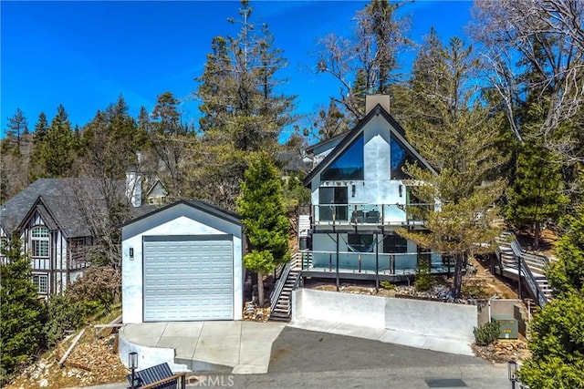 chalet / cabin featuring stairway, a detached garage, a balcony, driveway, and an outdoor structure