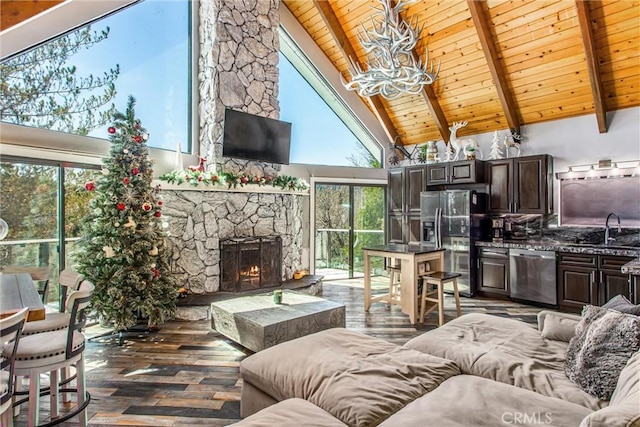 living area with dark wood-style floors, beamed ceiling, wooden ceiling, a stone fireplace, and high vaulted ceiling