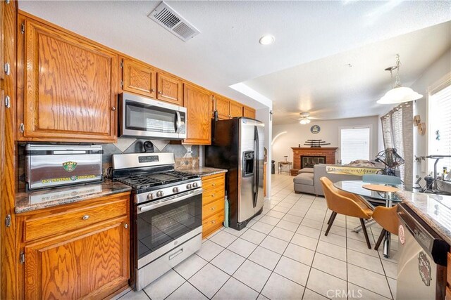 39240 Gunsmoke Ct, Palmdale, CA 93551 - kitchen featuring a brick fireplace, light tile patterned floors, a ceiling fan, visible vents, and appliances with stainless steel finishes