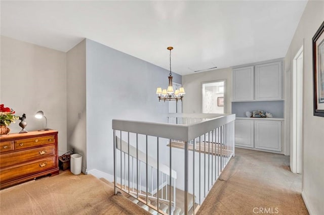 corridor featuring light carpet, an upstairs landing, baseboards, and a chandelier