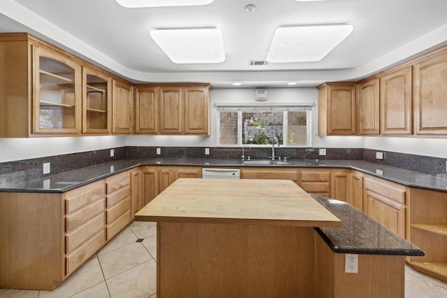 kitchen with glass insert cabinets, dark stone countertops, a sink, and a kitchen island