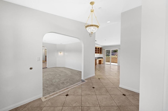 hall with light tile patterned floors, arched walkways, baseboards, and light carpet