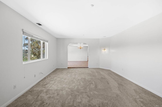 carpeted empty room with arched walkways, an inviting chandelier, visible vents, and baseboards