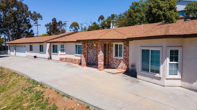 rear view of house featuring stucco siding, an attached garage, driveway, and brick siding