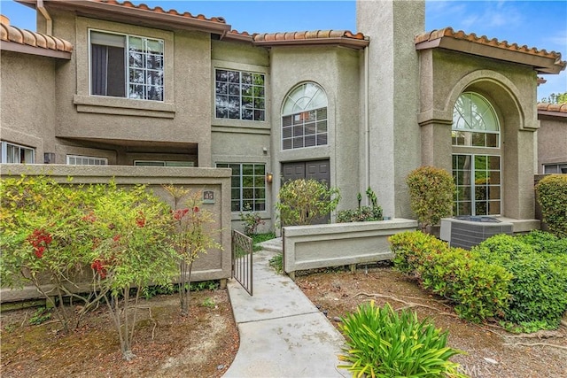 doorway to property with central air condition unit, fence, a tiled roof, and stucco siding