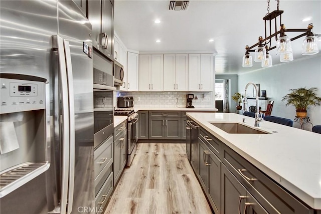 kitchen featuring stainless steel appliances, a sink, light wood finished floors, light countertops, and recessed lighting