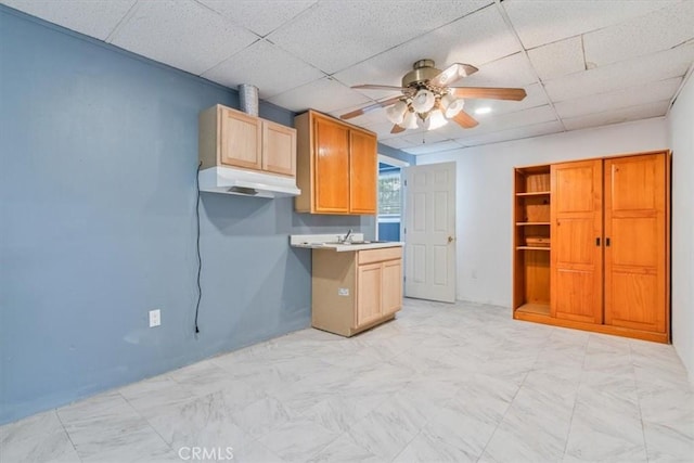 kitchen featuring a sink, a drop ceiling, ceiling fan, light countertops, and under cabinet range hood