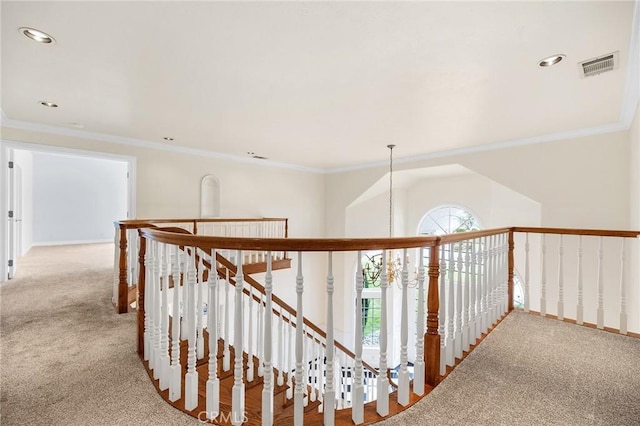 hallway with carpet, visible vents, crown molding, and an upstairs landing