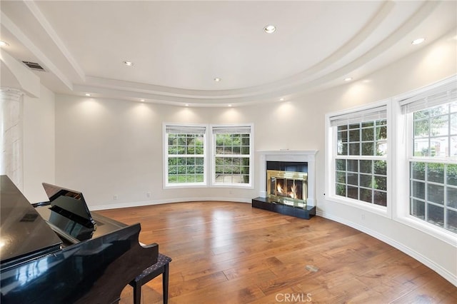 living area with ornate columns, a tray ceiling, a high end fireplace, visible vents, and hardwood / wood-style flooring
