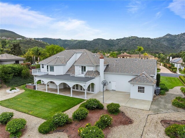 back of property with a balcony, covered porch, a mountain view, a yard, and stucco siding