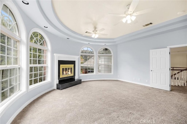 unfurnished living room featuring a wealth of natural light, carpet flooring, ceiling fan, and visible vents