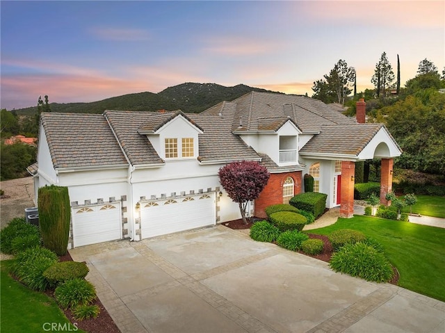 traditional home with a garage, concrete driveway, a chimney, a front yard, and stucco siding