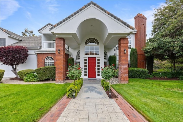 property entrance featuring a balcony, a lawn, a chimney, stucco siding, and brick siding