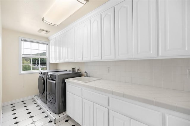 clothes washing area with washing machine and clothes dryer, a sink, baseboards, visible vents, and cabinet space