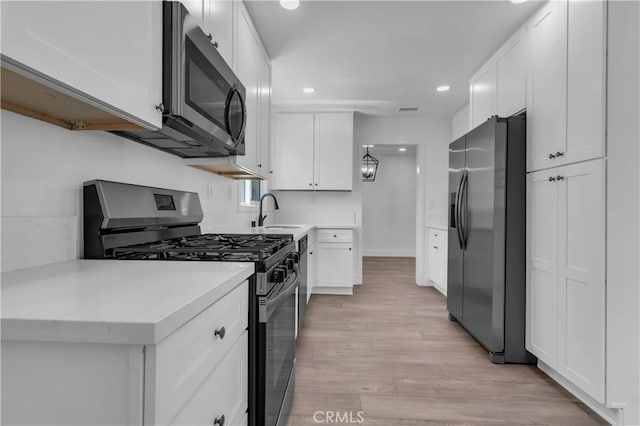 kitchen featuring white cabinets, stainless steel appliances, a sink, recessed lighting, and light countertops