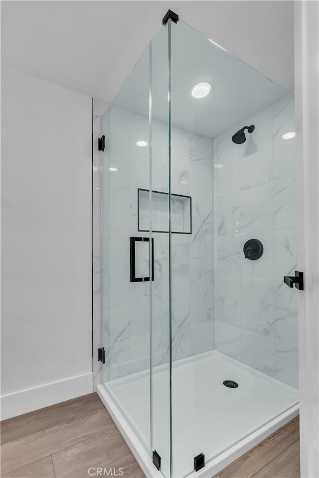 bathroom with wood finished floors, baseboards, and a marble finish shower