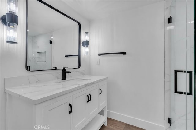 full bathroom featuring baseboards, wood finished floors, vanity, and a marble finish shower