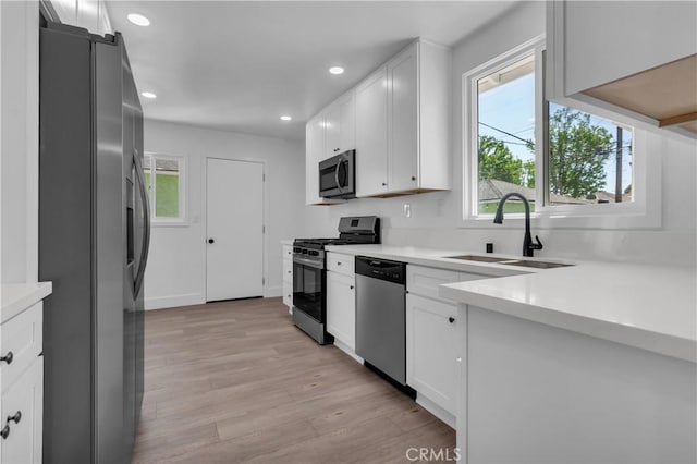 kitchen featuring light wood finished floors, plenty of natural light, appliances with stainless steel finishes, and a sink
