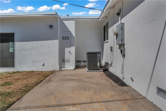 view of side of property with stucco siding, a patio, and central AC unit