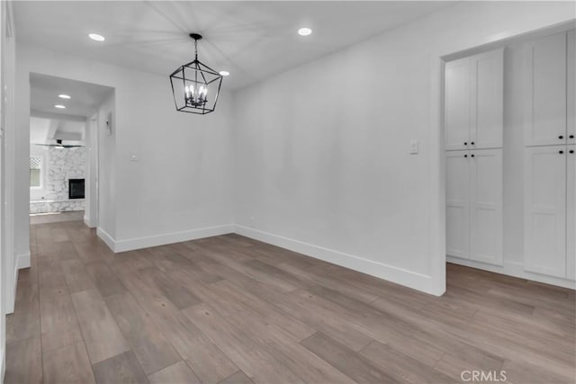 unfurnished dining area with light wood-type flooring, baseboards, recessed lighting, and a notable chandelier