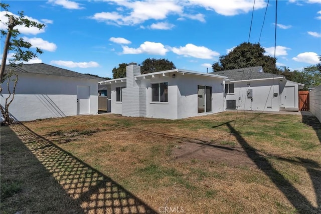 back of house featuring a chimney, central AC unit, fence, stucco siding, and a lawn