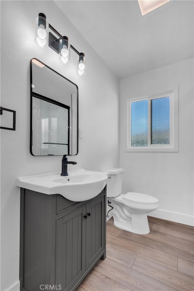 bathroom with baseboards, wood finished floors, vanity, and toilet