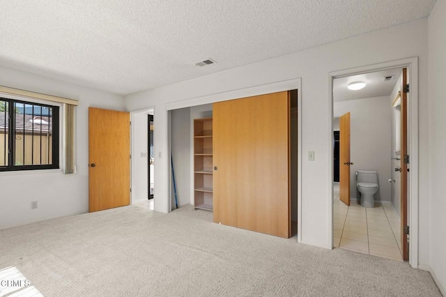 unfurnished bedroom with ensuite bathroom, a textured ceiling, a closet, carpet, and visible vents