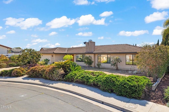 single story home with an attached garage, a tile roof, a chimney, and stucco siding