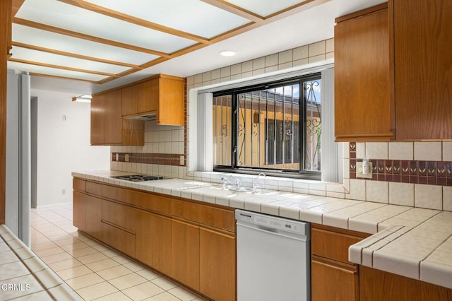 kitchen with a sink, light tile patterned flooring, backsplash, white dishwasher, and stovetop