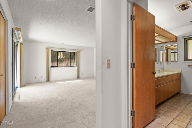 hallway with a textured ceiling, visible vents, light colored carpet, and a sink