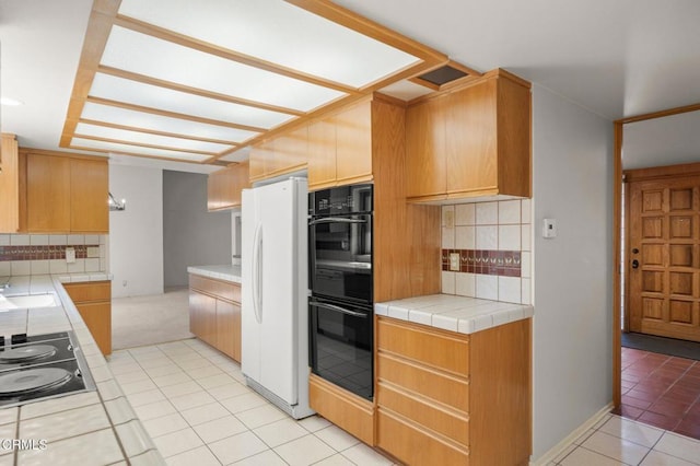 kitchen featuring tile countertops, a sink, light tile patterned flooring, black appliances, and tasteful backsplash