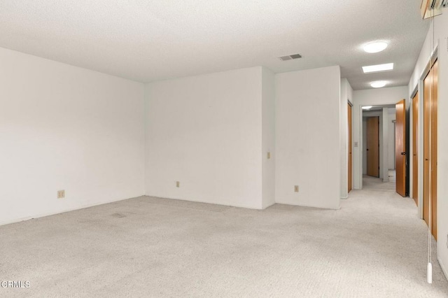 spare room with a textured ceiling, visible vents, and light carpet