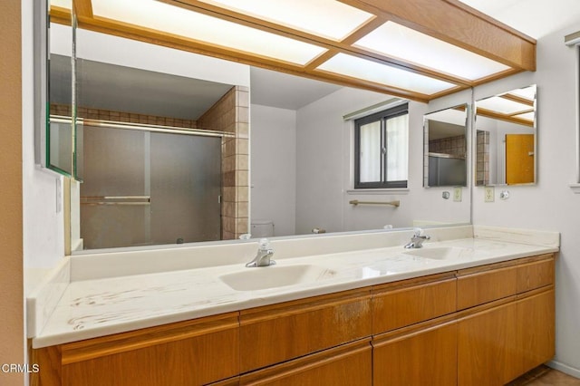 full bath featuring toilet, a shower with shower door, a sink, and double vanity