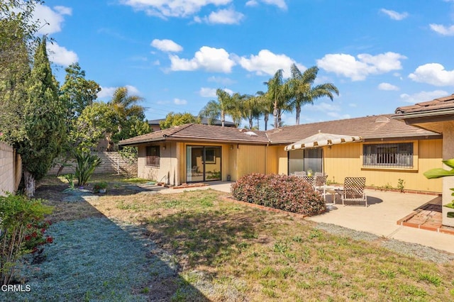 back of house with a lawn, fence, a tiled roof, and a patio