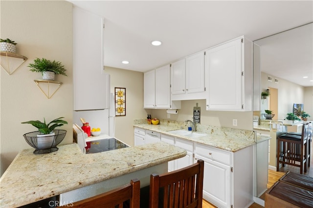 kitchen featuring light stone countertops, a sink, white cabinetry, and recessed lighting