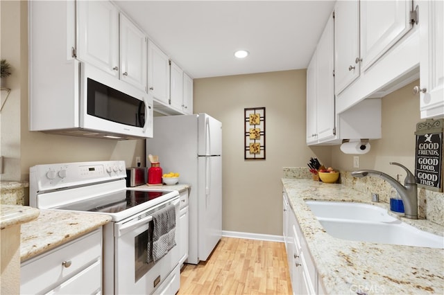 kitchen featuring recessed lighting, light wood finished floors, a sink, white appliances, and white cabinetry
