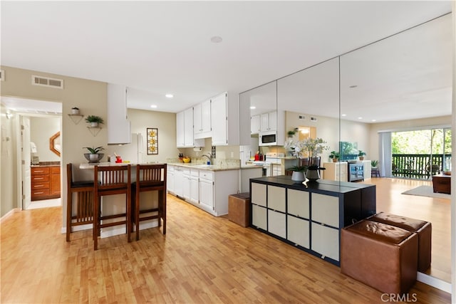 kitchen with light wood-type flooring, visible vents, white microwave, white cabinetry, and recessed lighting