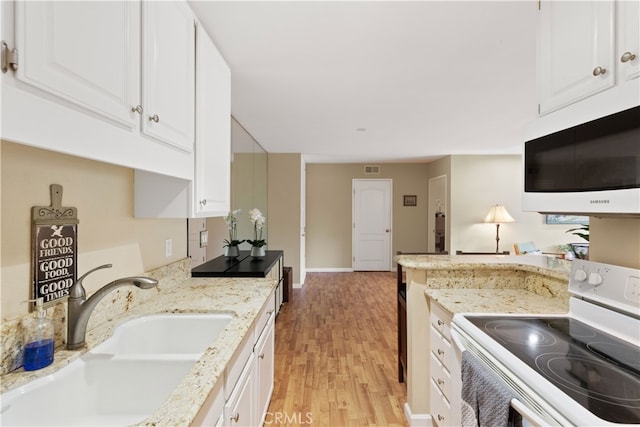 kitchen with white cabinets, light stone counters, a sink, white appliances, and light wood-style floors
