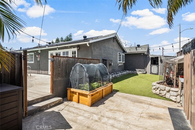 rear view of property with stucco siding, fence, a lawn, and a patio