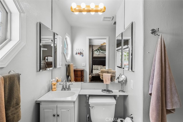 bathroom with toilet, visible vents, vanity, and a healthy amount of sunlight