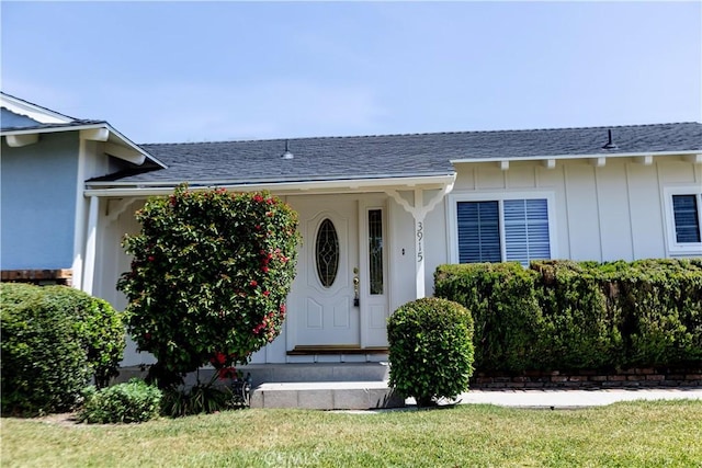 doorway to property with board and batten siding, a yard, and roof with shingles