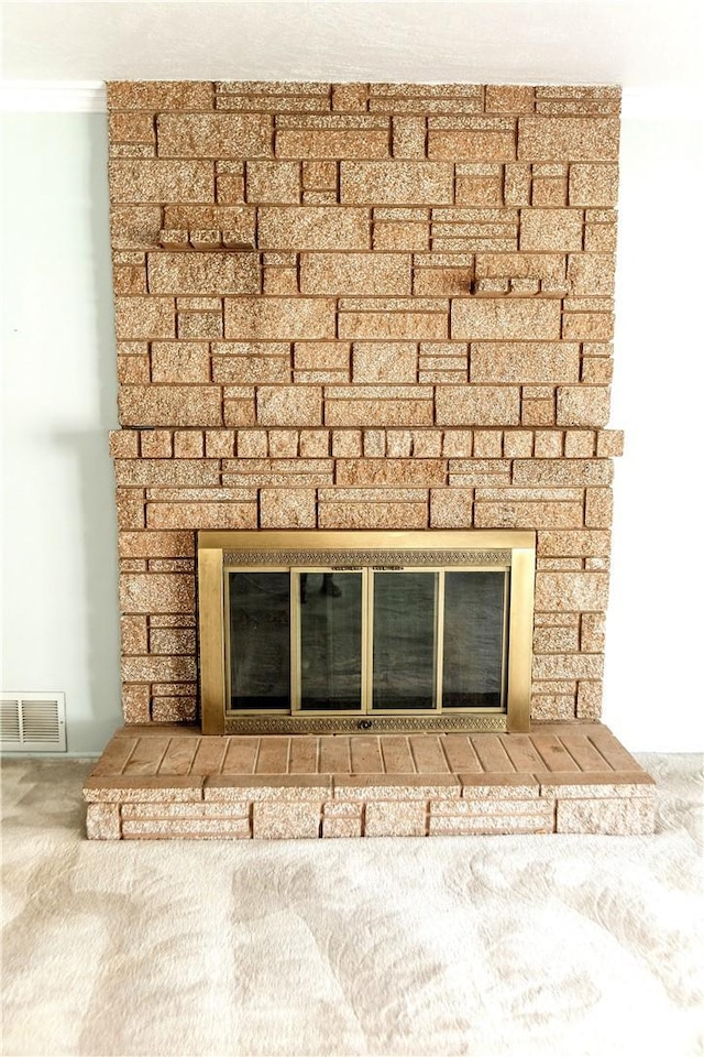 interior details featuring visible vents, crown molding, carpet flooring, and a stone fireplace