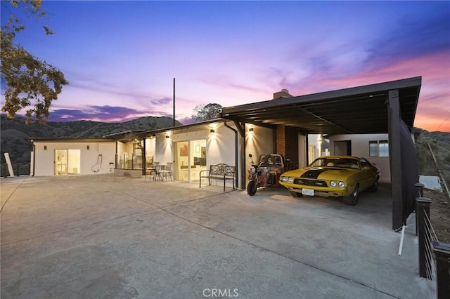 view of front of property featuring concrete driveway, a chimney, an attached carport, a mountain view, and stucco siding