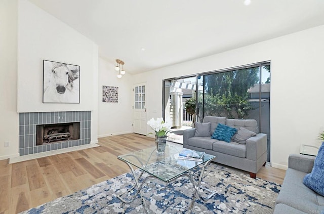 living area with vaulted ceiling, wood finished floors, a tiled fireplace, and baseboards