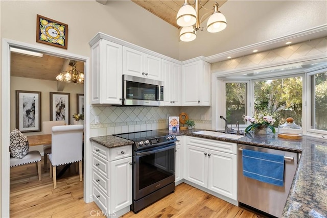 kitchen featuring vaulted ceiling, a sink, decorative backsplash, a chandelier, and appliances with stainless steel finishes