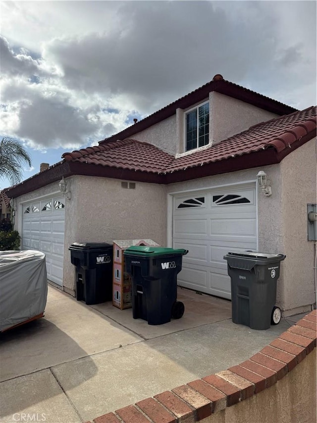 view of property exterior with a tile roof, stucco siding, and an attached garage